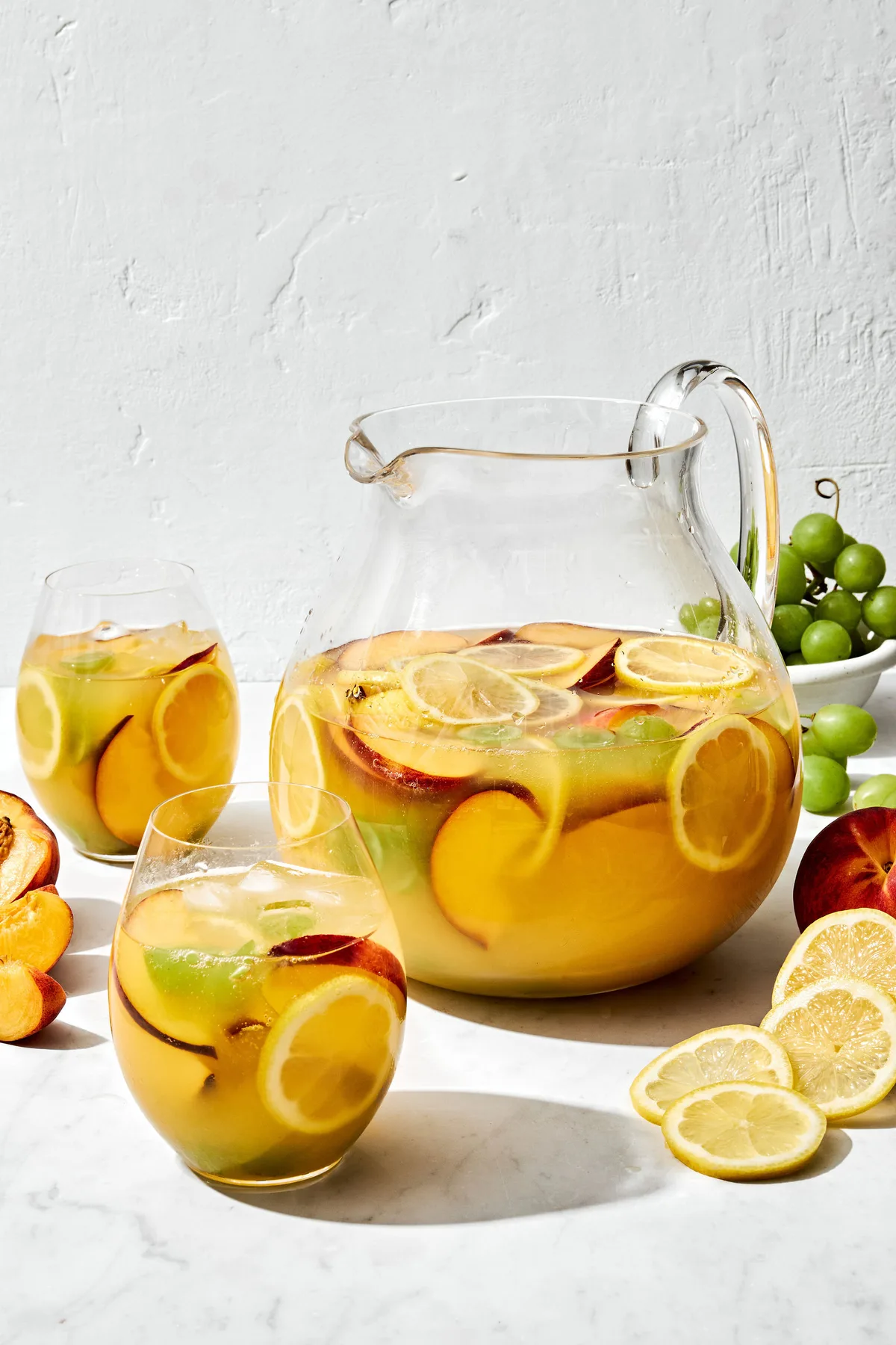 a large pitcher of white sangria filled with fruit slices, surrounded by glasses of sangria