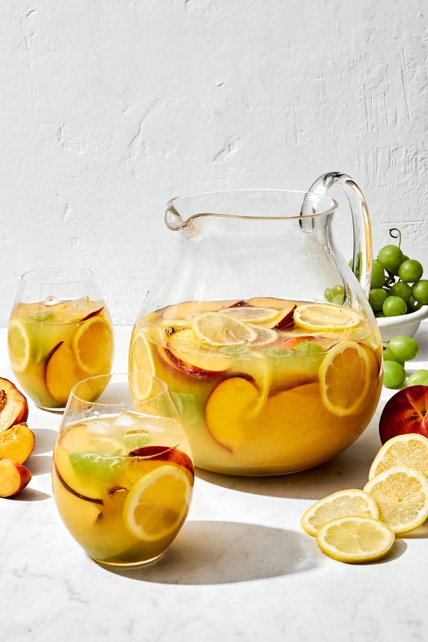 a large pitcher of white sangria filled with fruit slices, surrounded by glasses of sangria
