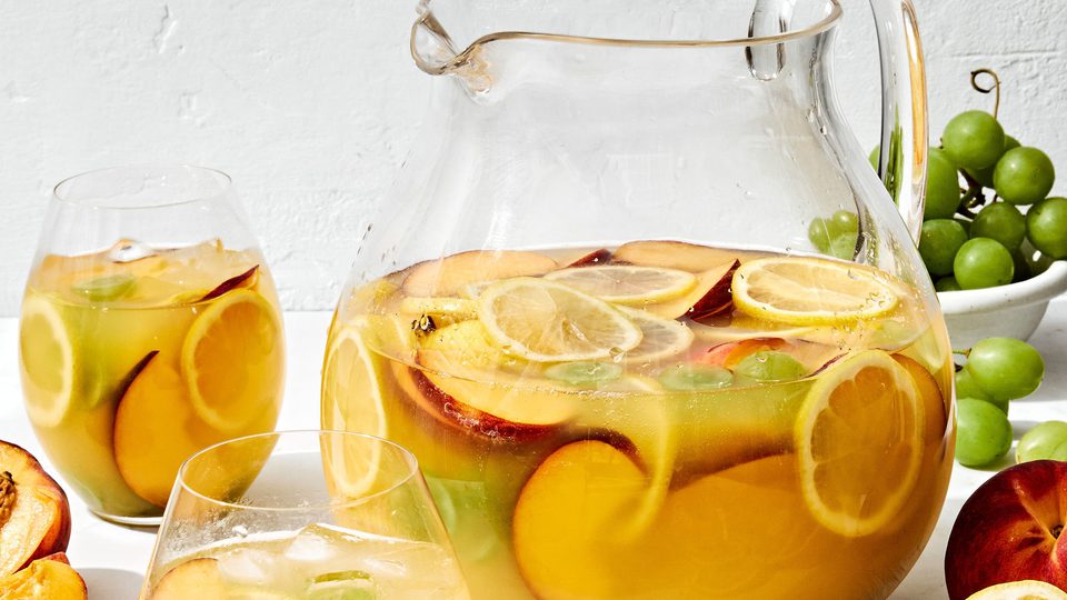 a large pitcher of white sangria filled with fruit slices, surrounded by glasses of sangria