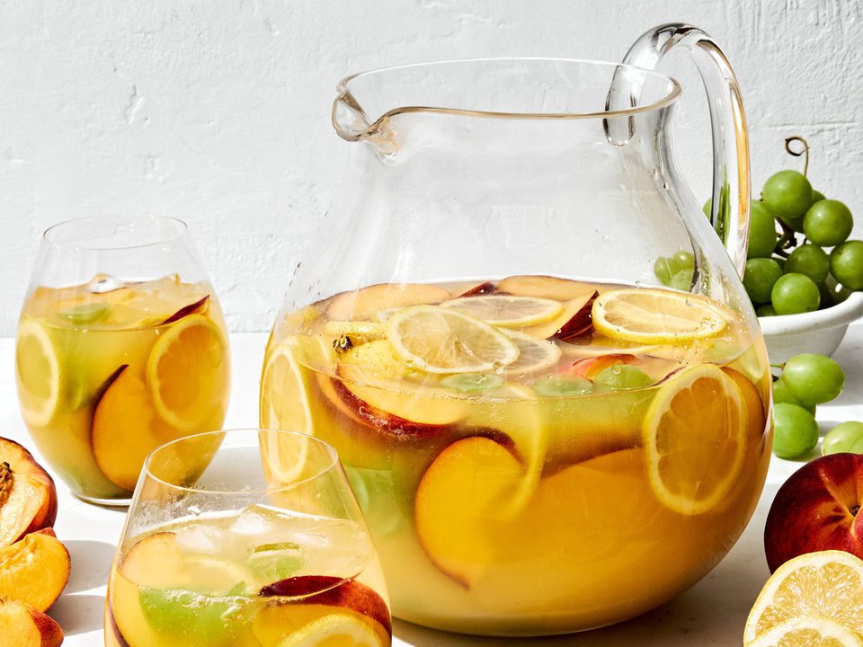 a large pitcher of white sangria filled with fruit slices, surrounded by glasses of sangria