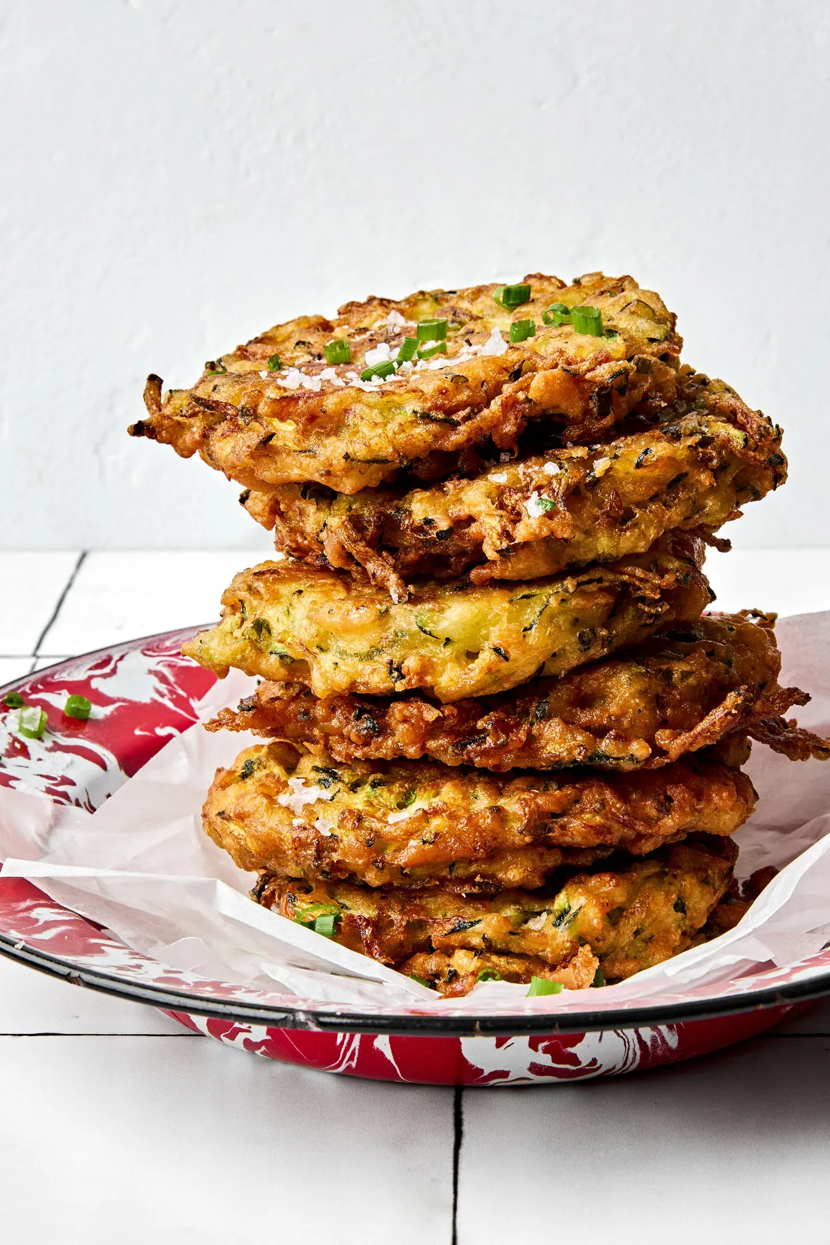A stack of golden-brown, homemade zucchini fritters arranged on a white plate.