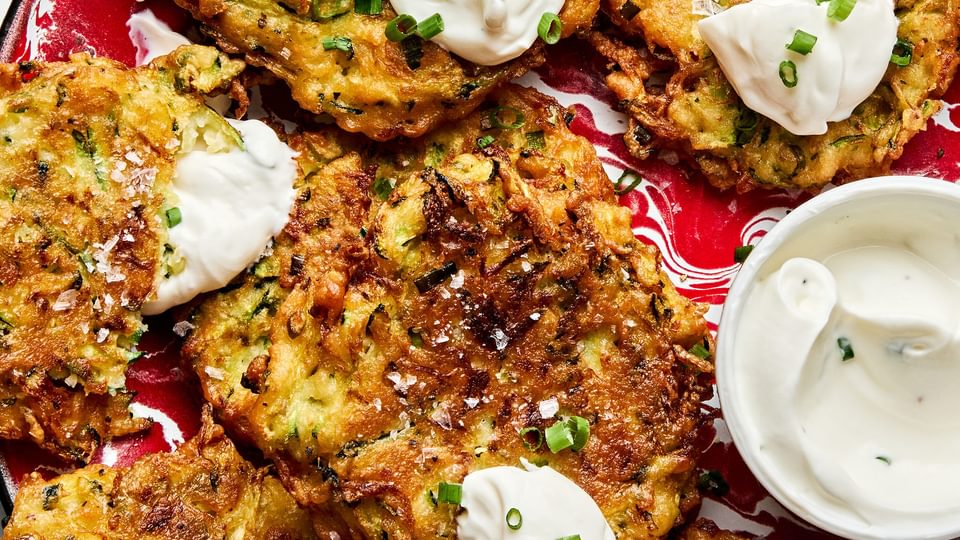 golden-brown homemade zucchini fritters with perfectly crispy on the edges on a plate served with sour cream