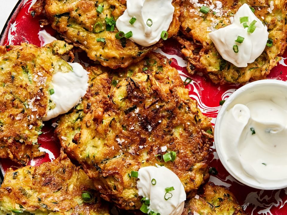 golden-brown homemade zucchini fritters with perfectly crispy on the edges on a plate served with sour cream