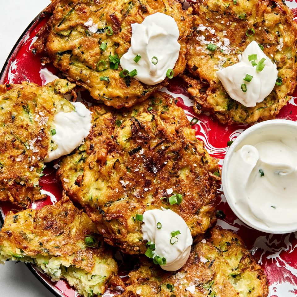 golden-brown homemade zucchini fritters with perfectly crispy on the edges on a plate served with sour cream