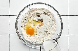 batter for zucchini fritters being made in a bowl with flour, baking powder, green onions, Parmesan, egg, milk and spices