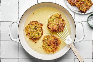 A skillet filled with sizzling oil, actively cooking several zucchini fritters until golden-brown with crispy edges