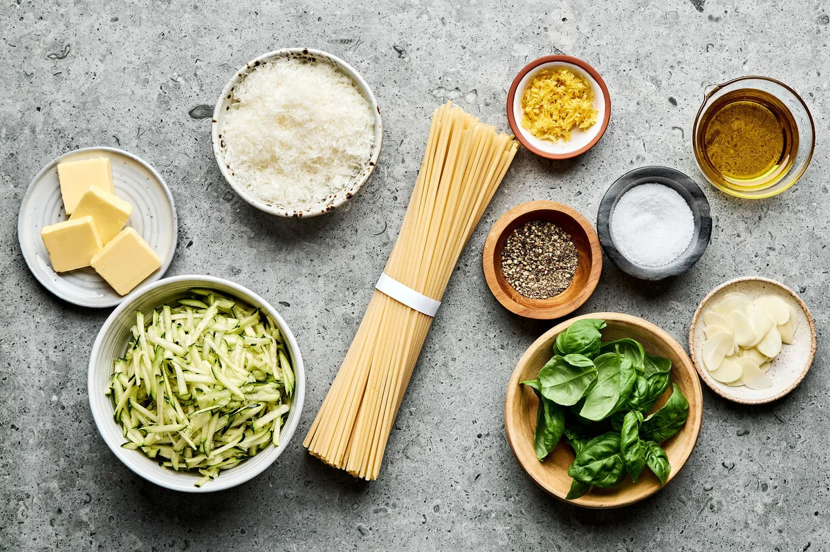 ingredients laid out for zucchini pasta including spaghetti, zucchini, Parmesan, garlic, lemon zest, butter, and basil