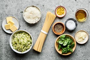 ingredients laid out for zucchini pasta including spaghetti, zucchini, Parmesan, garlic, lemon zest, butter, and basil