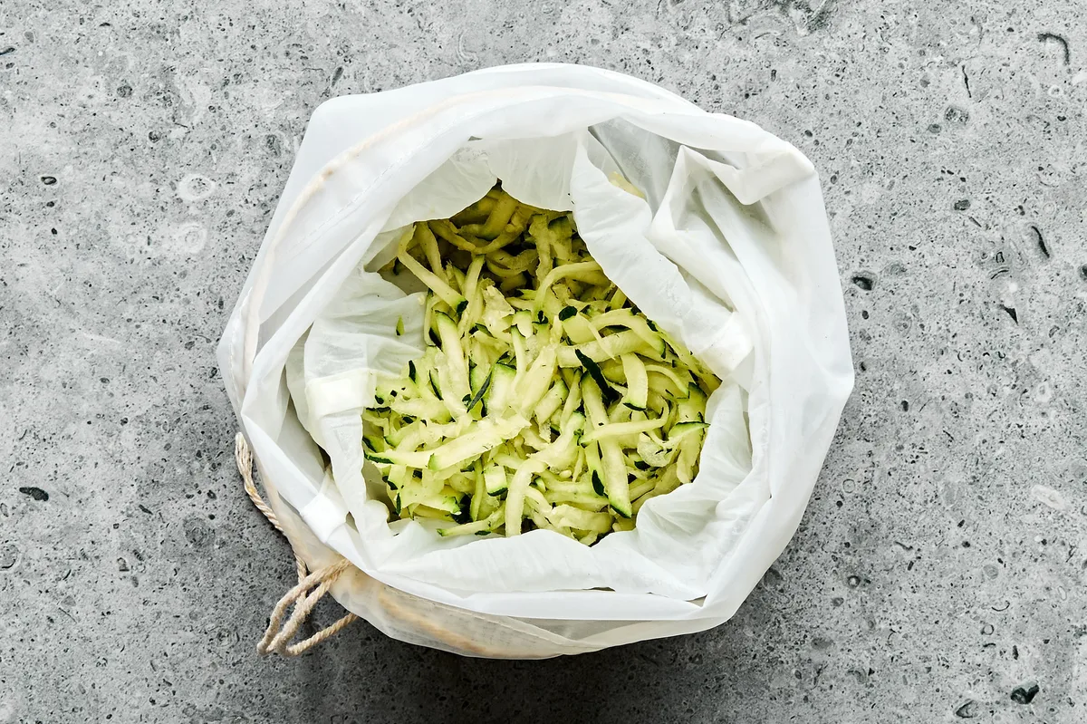 grated zucchini being strained in cheesecloth to draw out all the moisture before cooking