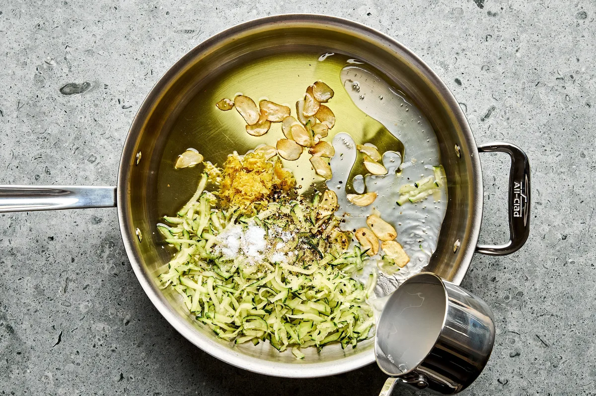 grated zucchini being cooked in a pan with olive oil, garlic, salt, pepper and lemon zest to make zucchini pasta
