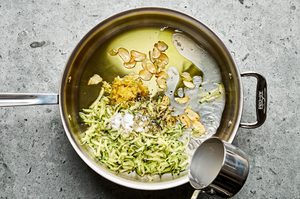 grated zucchini being cooked in a pan with olive oil, garlic, salt, pepper and lemon zest to make zucchini pasta