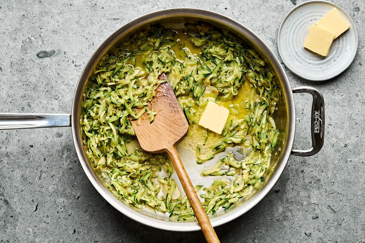 grated zucchini being cooked in a pan with butter, olive oil, garlic, salt, pepper and lemon zest to make zucchini pasta
