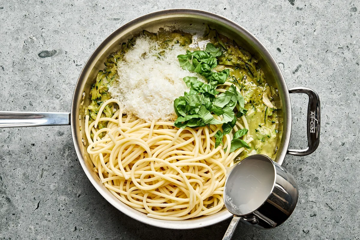 cooked spaghetti noodles being tossed with a creamy parmesan zucchini sauce in a pan