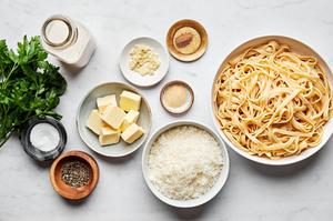 Butter, cream, garlic, garlic powder, nutmeg, Parmesan, parsley and noodles in prep bowls to make alfredo sauce