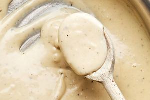 alfredo sauce being stirred n a skillet made with Butter, cream, garlic, garlic powder, nutmeg, and Parmesan