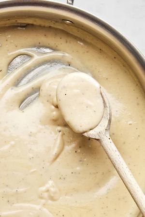 alfredo sauce being stirred n a skillet made with Butter, cream, garlic, garlic powder, nutmeg, and Parmesan