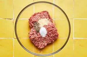 ground beed, slat, pepper and garlic powder in a glass bowl on a yellow tile surface