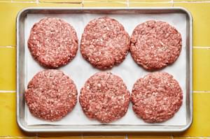 6 ground beef burger patties on a rimmed sheet pan