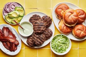buns, burgers, bacon, lettuce, avocado, red onion and jalapeño aioli in bowls to assemble avocado burgers with bacon
