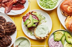 brioche buns, burgers, bacon, lettuce, avocado, red onion and jalapeño aioli in bowls to assemble avocado burgers with bacon
