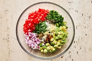 avocado, tomato, red onion, jalapeño, cilantro, lime juice and spices being combined in a glass bowl
