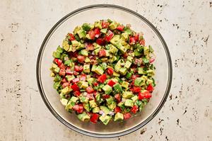 avocado, tomato, red onion, jalapeño, cilantro, lime juice and spices being tossed in a glass bowl
