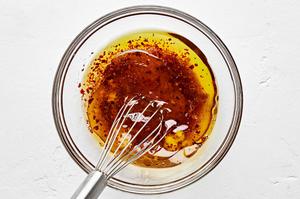 dressing made with vinegar, garlic, brown sugar, olive oil, pepper, and salt being whisked together in a bowl.