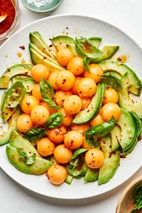 avocado and melon salad with fresh basil and drizzled with homemade dressing on a serving platter