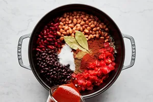 beef, pork, onion, peppers, garlic, spices, black, kidney and pinto beans being cooked in a large soup pot