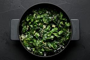 onions, garlic and swiss chard being cooked in olive oil in a skillet