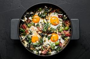 baked eggs with swiss chard and green olives in a skillet topped with toasted panko