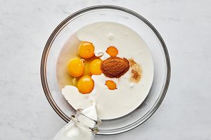eggs, milk, cream, vanilla and cinnamon being added to a glass bowl to use in baked french toast, the perfect weekend brunch