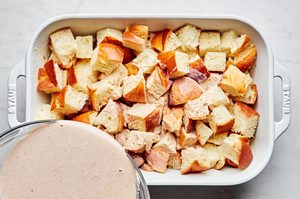 egg and cream mixture being poured over torn challah bread in a baking dish to make baked french toast, the perfect brunch