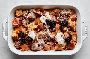 homemade baked french toast made with challah bread in a baking dish topped with dollops of whipped cream and blackberries