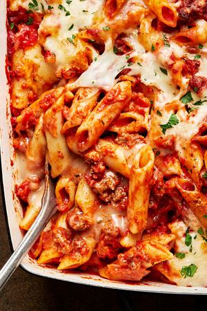 homemade baked Mostaccioli topped with melted mozzarella cheese and sprinkled with parsley being scooped out of a pan