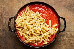 cooked Mostaccioli pasta being stirred into pasta sauce in a large pot