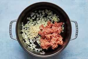 olive oil, onion, garlic and Italian sausage being cooked in a large pot