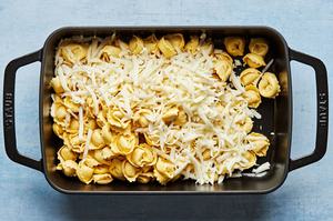 fresh tortellini in a baking dish being sprinkled with shredded mozzarella cheese