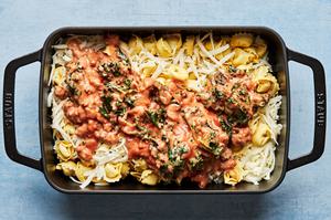 tortellini, mozzarella cheese and homemade sauce being combined in a baking dish to make baked tortellini