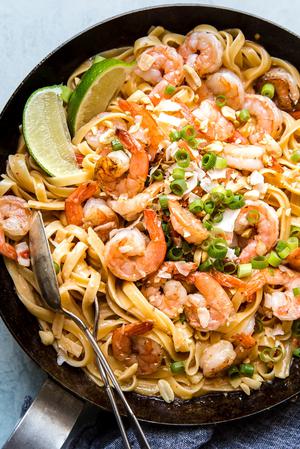 bang bang shrimp pasta in a dish with green onions and limes