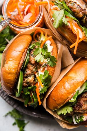 3 pork banh mi burgers on a plate with pickled veggies, cilantro and basil