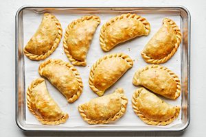homemade beef empanadas filled with potato, onion, carrot, celery, peas and spices on a baking sheet fresh out of the oven