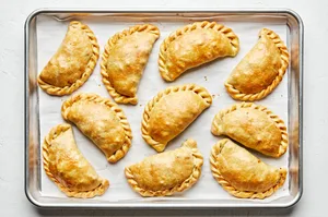 homemade beef empanadas filled with potato, onion, carrot, celery, peas and spices on a baking sheet fresh out of the oven