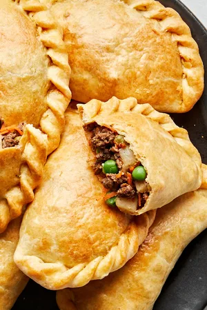 Plate of homemade beef empanadas with golden flaky crust and savory ground beef filling with potatoes, carrots, peas & onions