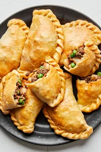 Plate of homemade beef empanadas with golden flaky crust and savory ground beef filling with potatoes, carrots, peas & onions