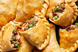 Plate of homemade beef empanadas with golden flaky crust and savory ground beef filling with potatoes, carrots, peas & onions