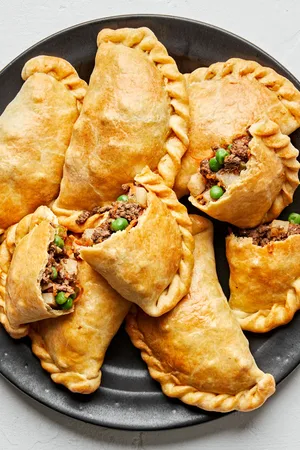Plate of homemade beef empanadas with golden flaky crust and savory ground beef filling with potatoes, carrots, peas & onions