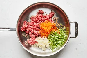 ground beef, onions, carrots and celery being cooked in a skillet to make savory ground beef empanada filling