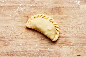 an uncooked beef empanada with savory ground beef filling and rolled edges on a bread board
