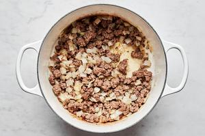 ground beef and chopped onion being cooked in olive oil in a large pot